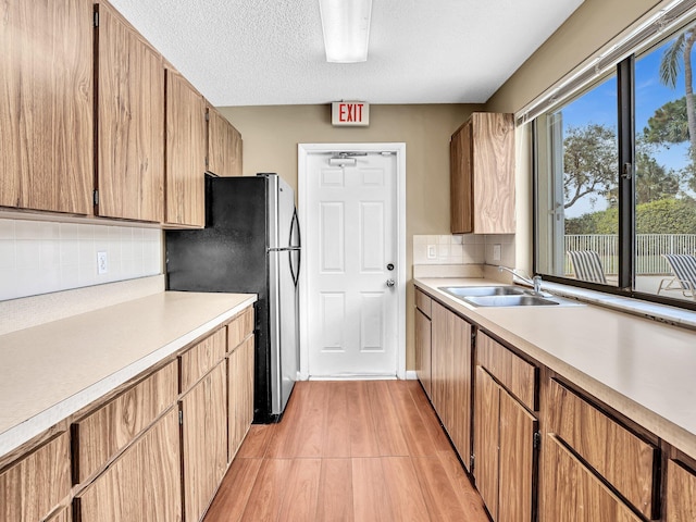 kitchen with sink, stainless steel refrigerator, light hardwood / wood-style floors, a textured ceiling, and decorative backsplash