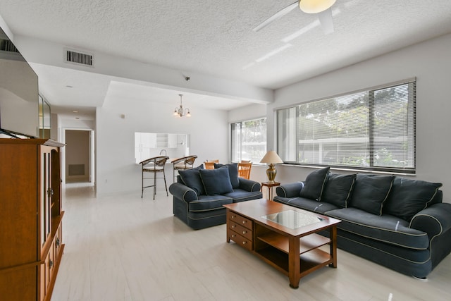 living room with a textured ceiling, a wealth of natural light, and ceiling fan with notable chandelier