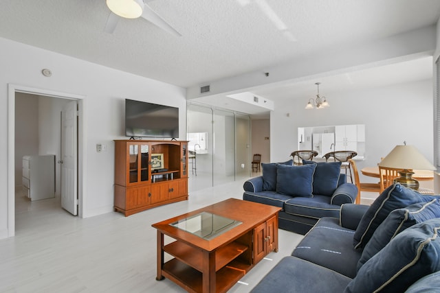 living room featuring ceiling fan with notable chandelier and a textured ceiling