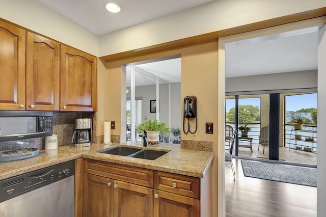 kitchen with tasteful backsplash, dishwasher, light stone counters, wood-type flooring, and sink