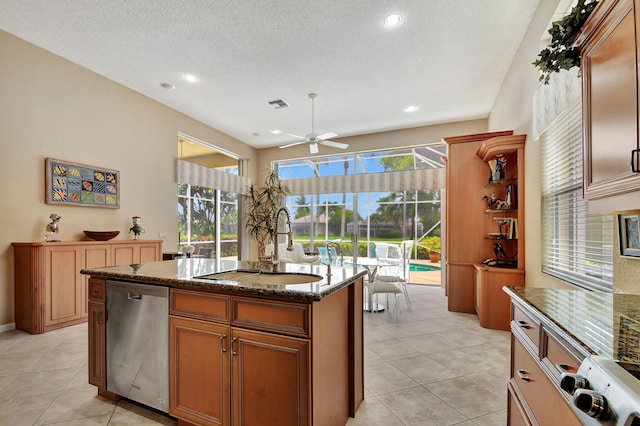 kitchen with an island with sink, sink, dark stone counters, stainless steel dishwasher, and light tile patterned floors