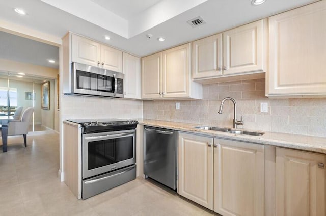 kitchen with appliances with stainless steel finishes, tasteful backsplash, a sink, and light stone countertops