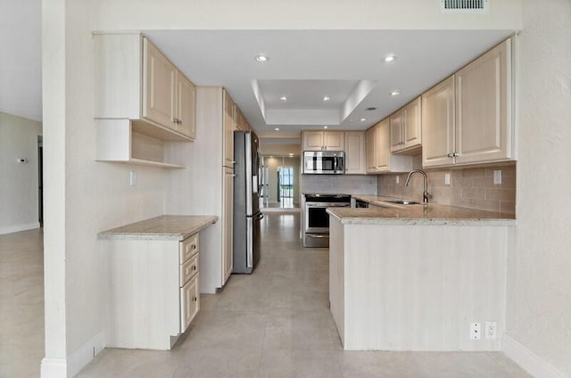 kitchen with stainless steel appliances, a raised ceiling, decorative backsplash, light brown cabinets, and a sink