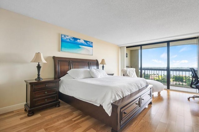 bedroom with access to exterior, light wood finished floors, a textured ceiling, a wall of windows, and baseboards