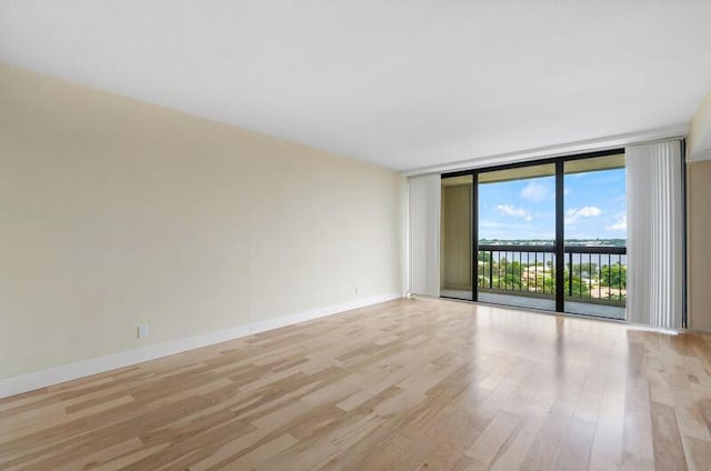 unfurnished room with a water view, light wood-type flooring, baseboards, and floor to ceiling windows