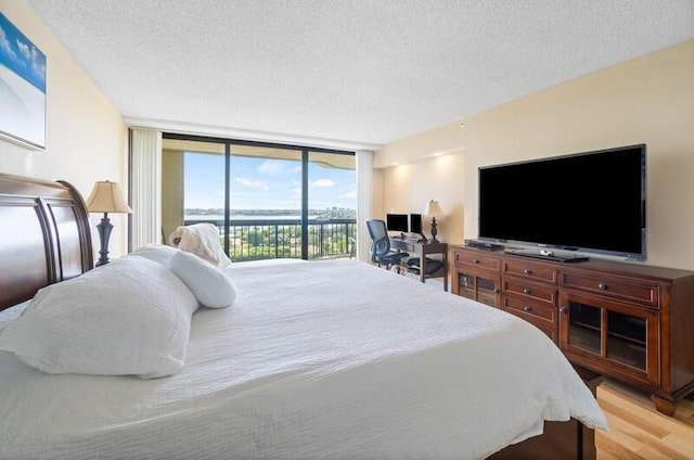 bedroom featuring access to outside, light wood-style flooring, expansive windows, and a textured ceiling