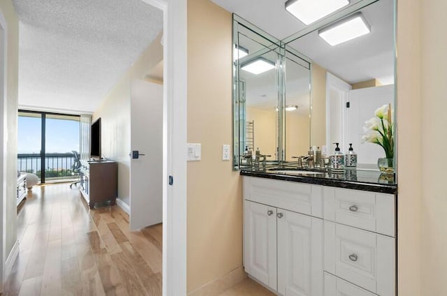 bathroom featuring baseboards, wood finished floors, a wall of windows, a textured ceiling, and vanity