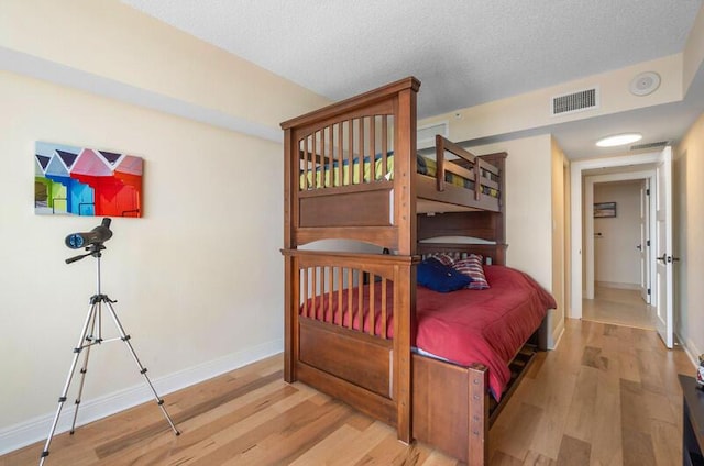 bedroom with light wood-style floors, visible vents, a textured ceiling, and baseboards