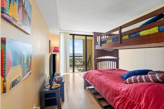 bedroom with light wood-style floors, access to outside, floor to ceiling windows, and a textured ceiling