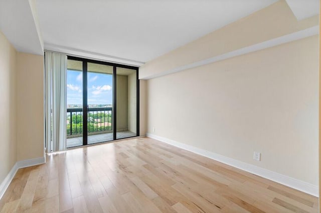 spare room with baseboards, floor to ceiling windows, and light wood-style flooring