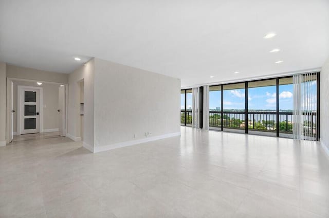 unfurnished room with recessed lighting, a wall of windows, a water view, and baseboards