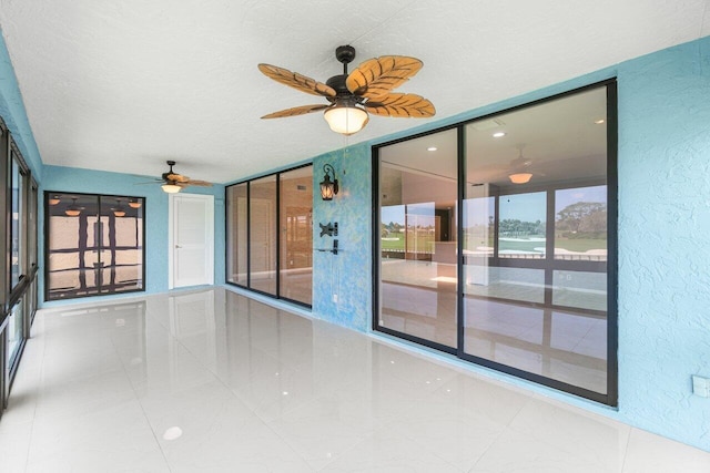 spare room featuring a ceiling fan, a textured wall, and a textured ceiling