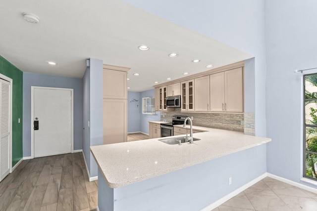 kitchen featuring glass insert cabinets, a sink, appliances with stainless steel finishes, and a peninsula