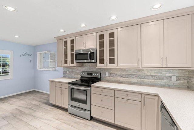 kitchen with recessed lighting, decorative backsplash, appliances with stainless steel finishes, glass insert cabinets, and baseboards