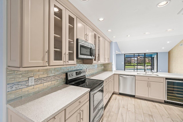 kitchen featuring backsplash, appliances with stainless steel finishes, glass insert cabinets, a sink, and beverage cooler