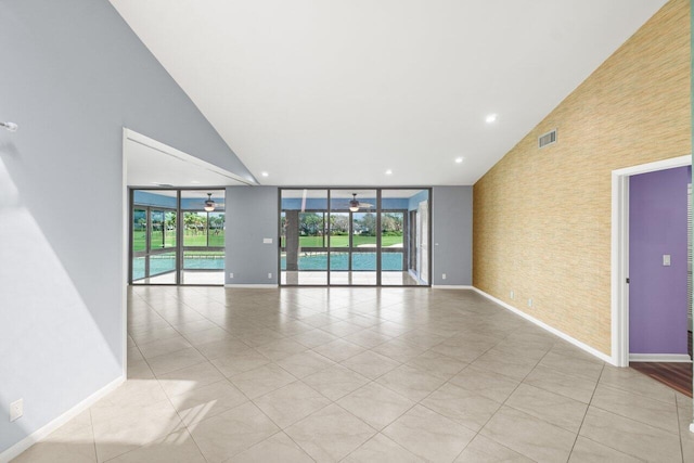 spare room featuring high vaulted ceiling, a ceiling fan, brick wall, a wall of windows, and baseboards