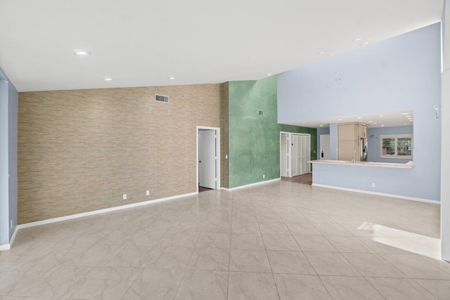 unfurnished living room featuring baseboards, visible vents, a towering ceiling, an accent wall, and recessed lighting