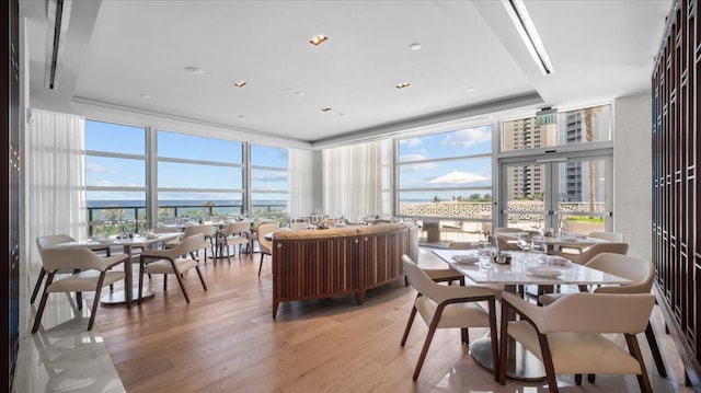 dining room featuring light hardwood / wood-style flooring, expansive windows, and a water view