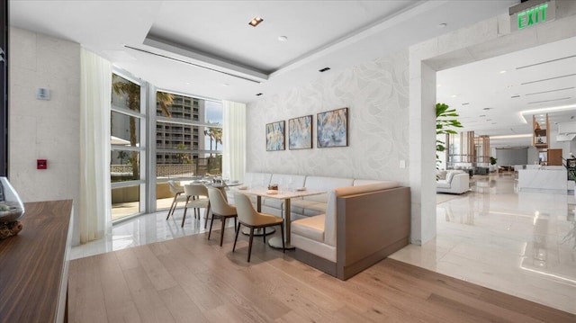 living room featuring a healthy amount of sunlight, light hardwood / wood-style flooring, a wall of windows, and a tray ceiling