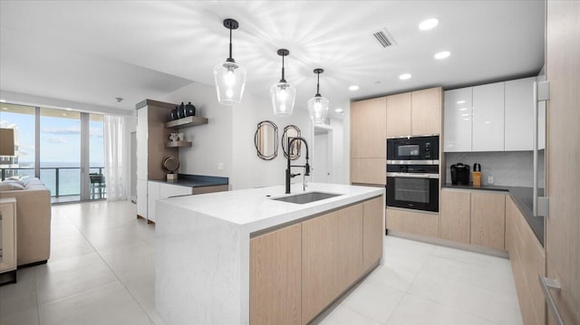 kitchen featuring pendant lighting, an island with sink, white cabinets, oven, and a water view