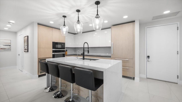 kitchen featuring sink, black microwave, an island with sink, decorative light fixtures, and oven