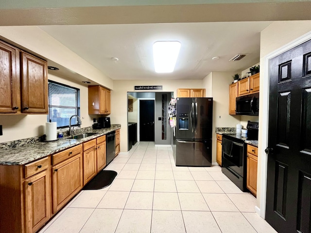 kitchen with light tile patterned flooring, sink, black appliances, and dark stone countertops