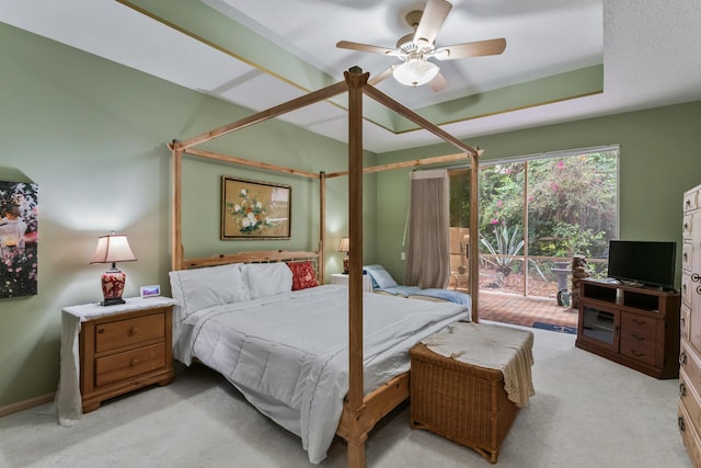 carpeted bedroom with ceiling fan, a tray ceiling, and access to exterior