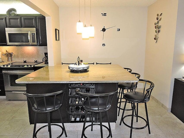 kitchen featuring hanging light fixtures, light stone counters, a breakfast bar area, appliances with stainless steel finishes, and a center island