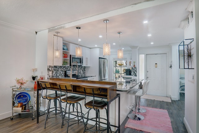 kitchen featuring kitchen peninsula, appliances with stainless steel finishes, a kitchen bar, white cabinetry, and hanging light fixtures