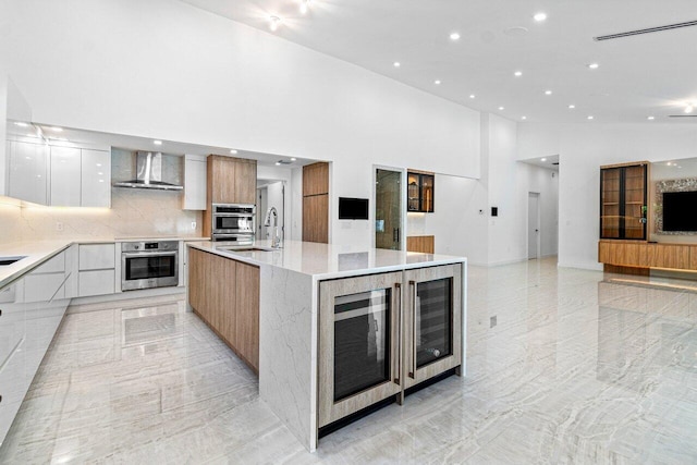 kitchen with a spacious island, light stone counters, white cabinets, decorative backsplash, and wall chimney range hood