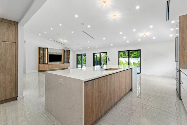 kitchen featuring a spacious island, lofted ceiling, light stone countertops, and sink