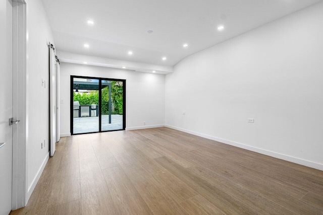 unfurnished room with lofted ceiling, a barn door, and light wood-type flooring