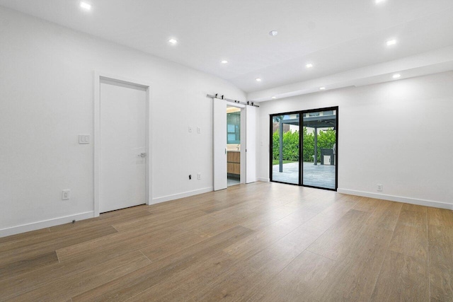 empty room with a barn door, vaulted ceiling, and light wood-type flooring