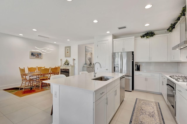 kitchen with appliances with stainless steel finishes, white cabinetry, an island with sink, sink, and light tile patterned flooring