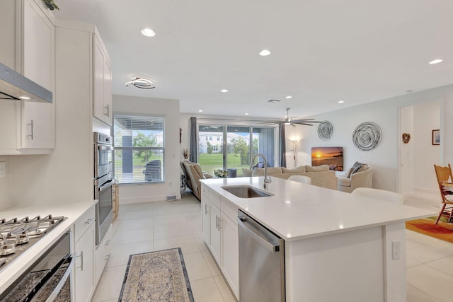 kitchen with white cabinetry, wall chimney range hood, stainless steel appliances, sink, and a kitchen island with sink