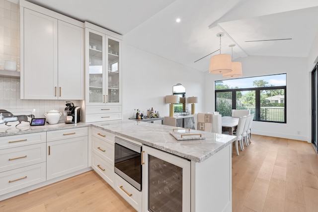 kitchen featuring stainless steel microwave, tasteful backsplash, beverage cooler, light hardwood / wood-style floors, and light stone countertops