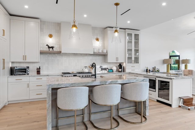 kitchen featuring light hardwood / wood-style flooring, light stone counters, premium range hood, backsplash, and wine cooler