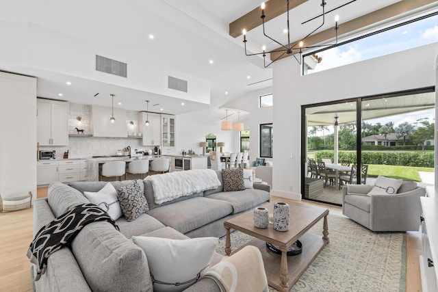 living room featuring light hardwood / wood-style floors, a notable chandelier, beamed ceiling, and a towering ceiling