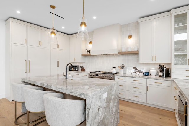 kitchen with white cabinetry, light wood-type flooring, backsplash, light stone counters, and a kitchen island with sink