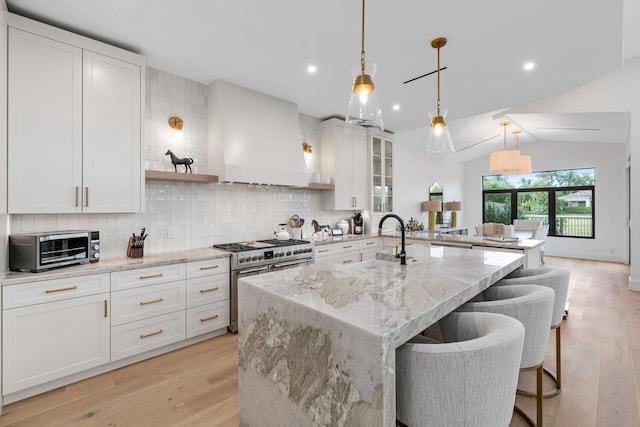 kitchen featuring light wood-type flooring, an island with sink, range with two ovens, decorative backsplash, and sink