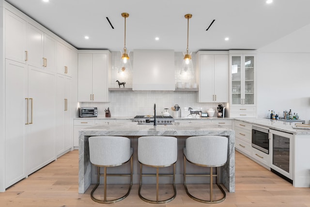 kitchen with light wood-type flooring, decorative backsplash, beverage cooler, and custom exhaust hood