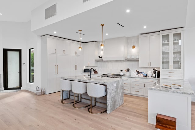 kitchen featuring white cabinetry, backsplash, light hardwood / wood-style floors, and light stone countertops