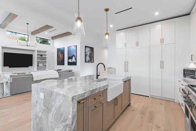 kitchen with beamed ceiling, light hardwood / wood-style flooring, white cabinets, and a large island with sink