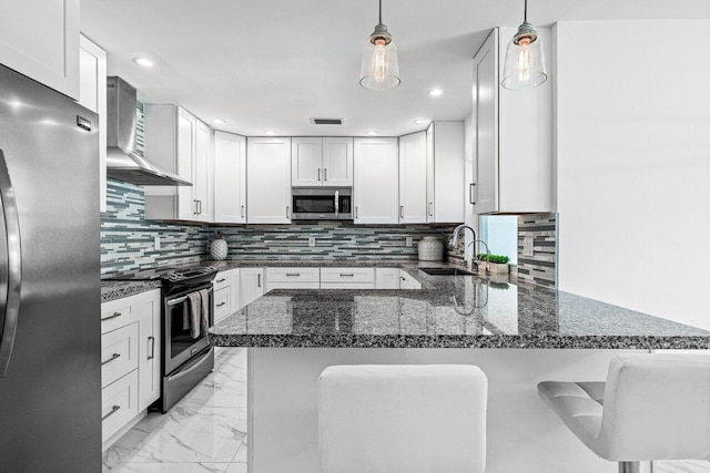 kitchen with decorative backsplash, appliances with stainless steel finishes, a kitchen bar, kitchen peninsula, and wall chimney range hood