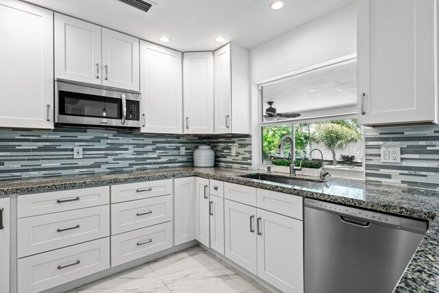 kitchen featuring tasteful backsplash, appliances with stainless steel finishes, white cabinetry, dark stone counters, and sink