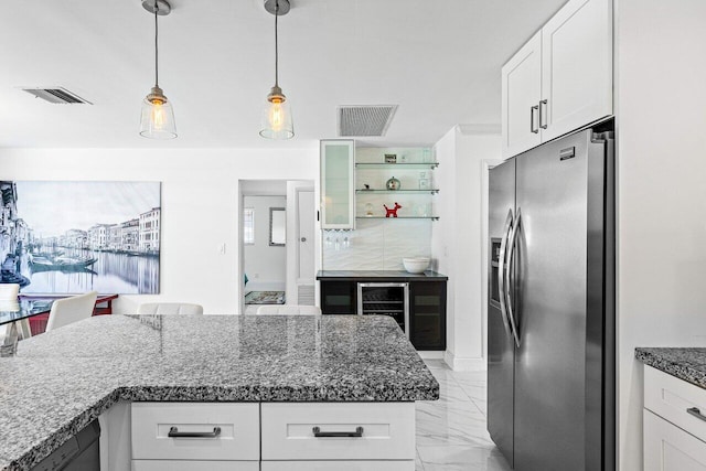 kitchen with white cabinetry, dark stone countertops, stainless steel fridge, light tile patterned floors, and decorative light fixtures