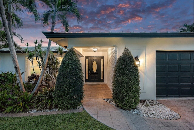 exterior entry at dusk with stucco siding and an attached garage