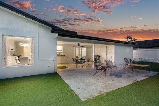 patio terrace at dusk with fence, a ceiling fan, and outdoor dining area