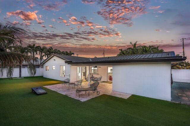 back house at dusk with a lawn and a patio