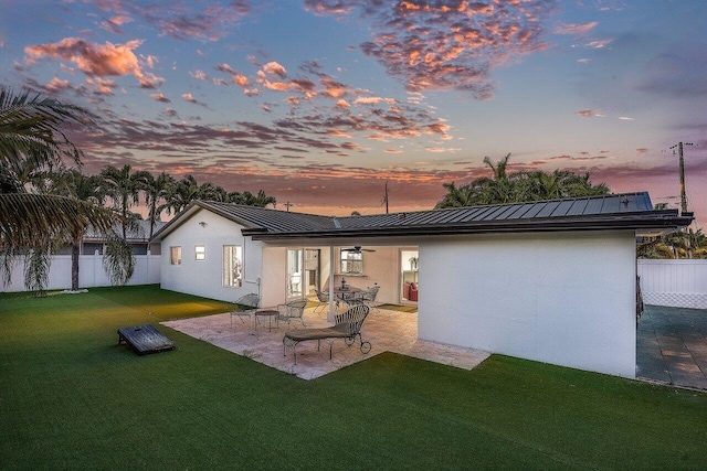 back of property at dusk with stucco siding, a lawn, a standing seam roof, fence, and metal roof